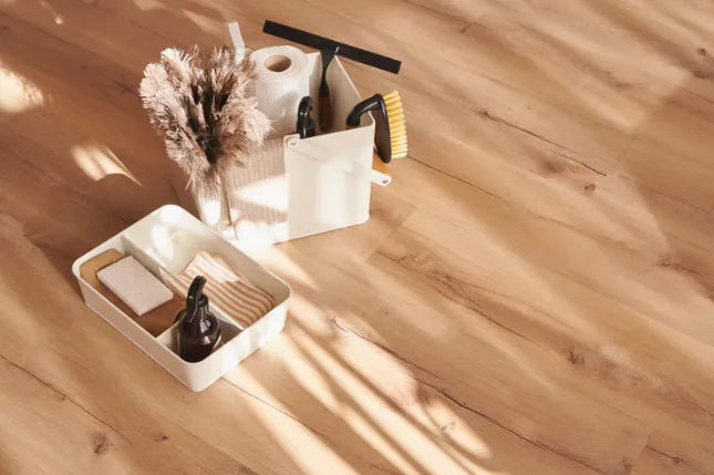 Cleaning supplies in caddies on a sunlit wooden floor